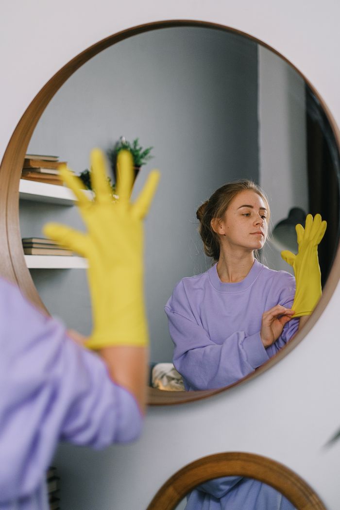 gallery-01 A woman wearing yellow gloves is reflected in a wall mirror indoors, exuding a serene expression.