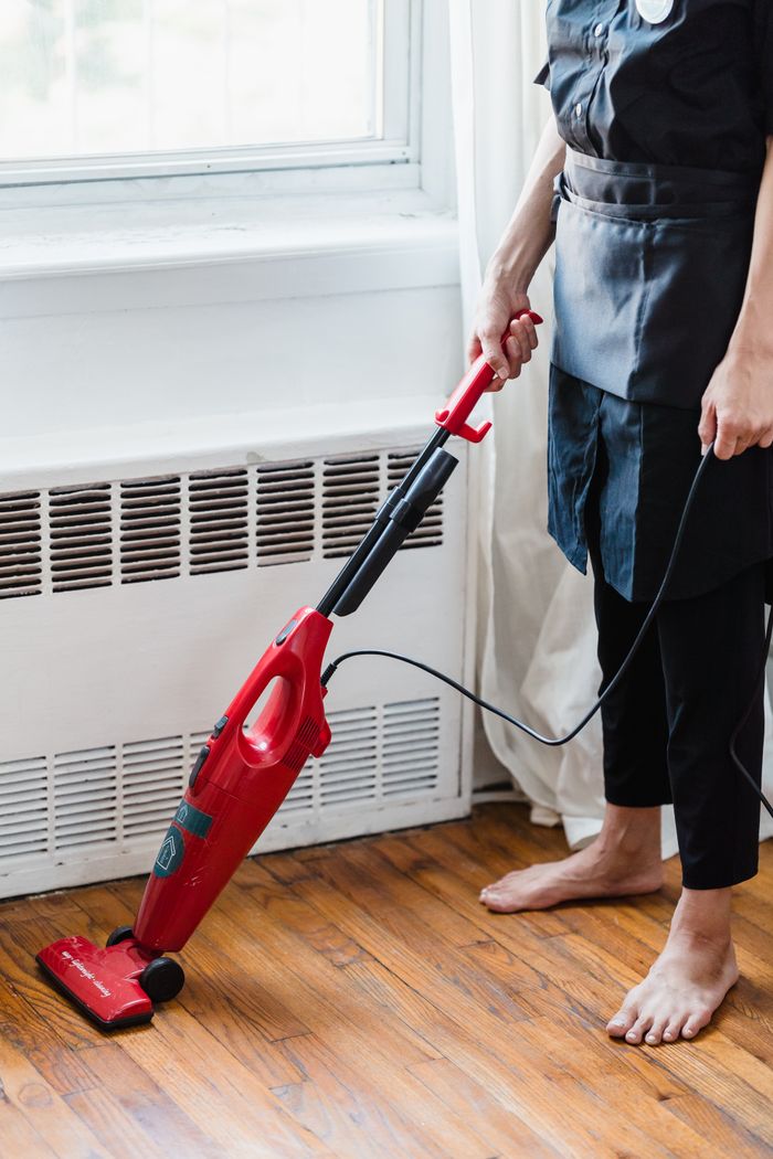 home-img Person cleaning wooden floor with red vacuum cleaner in a well-lit room.